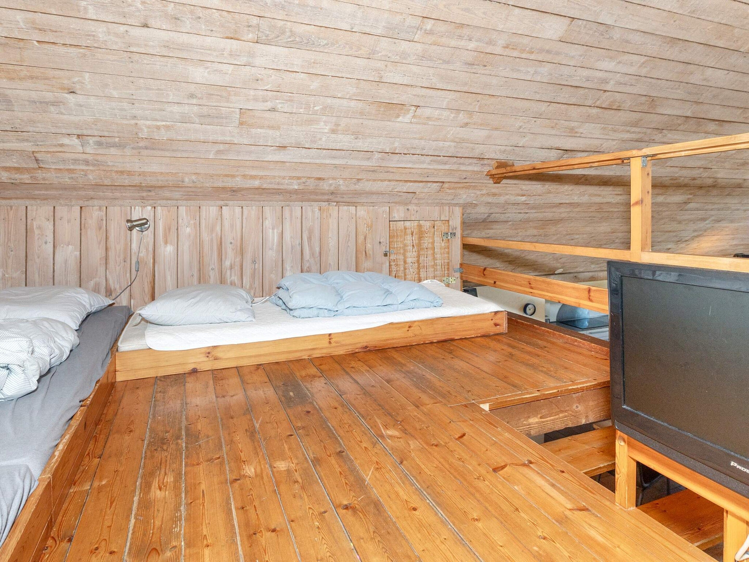 Habitación pequeña con una cama litera, una cama individual y un televisor sobre un atril de madera.