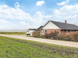 Una casa rural con un camino de tierra que la lleva a ella, rodeada de campos y un cielo despejado.