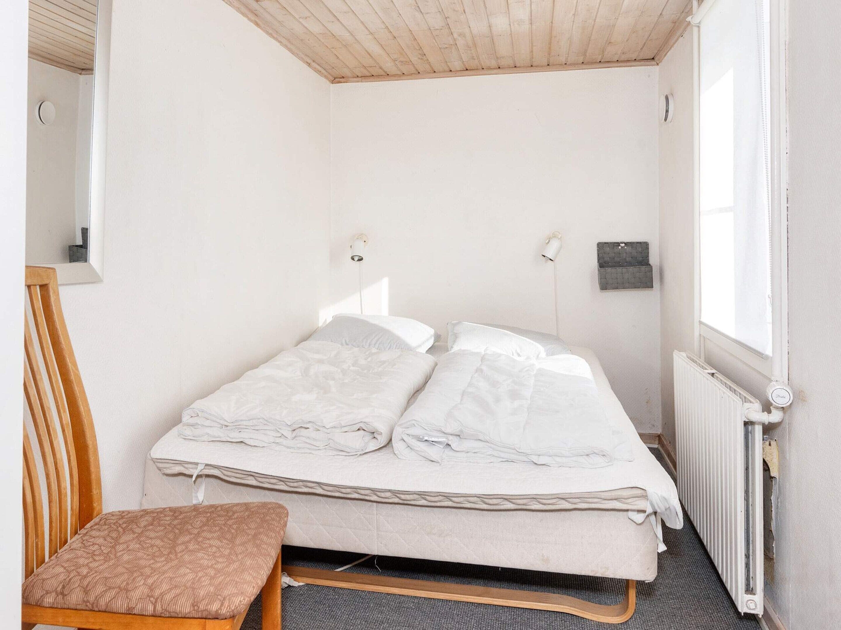 En enkeltseng med hvid dyne, en træstol, et lille bord og en radiator.