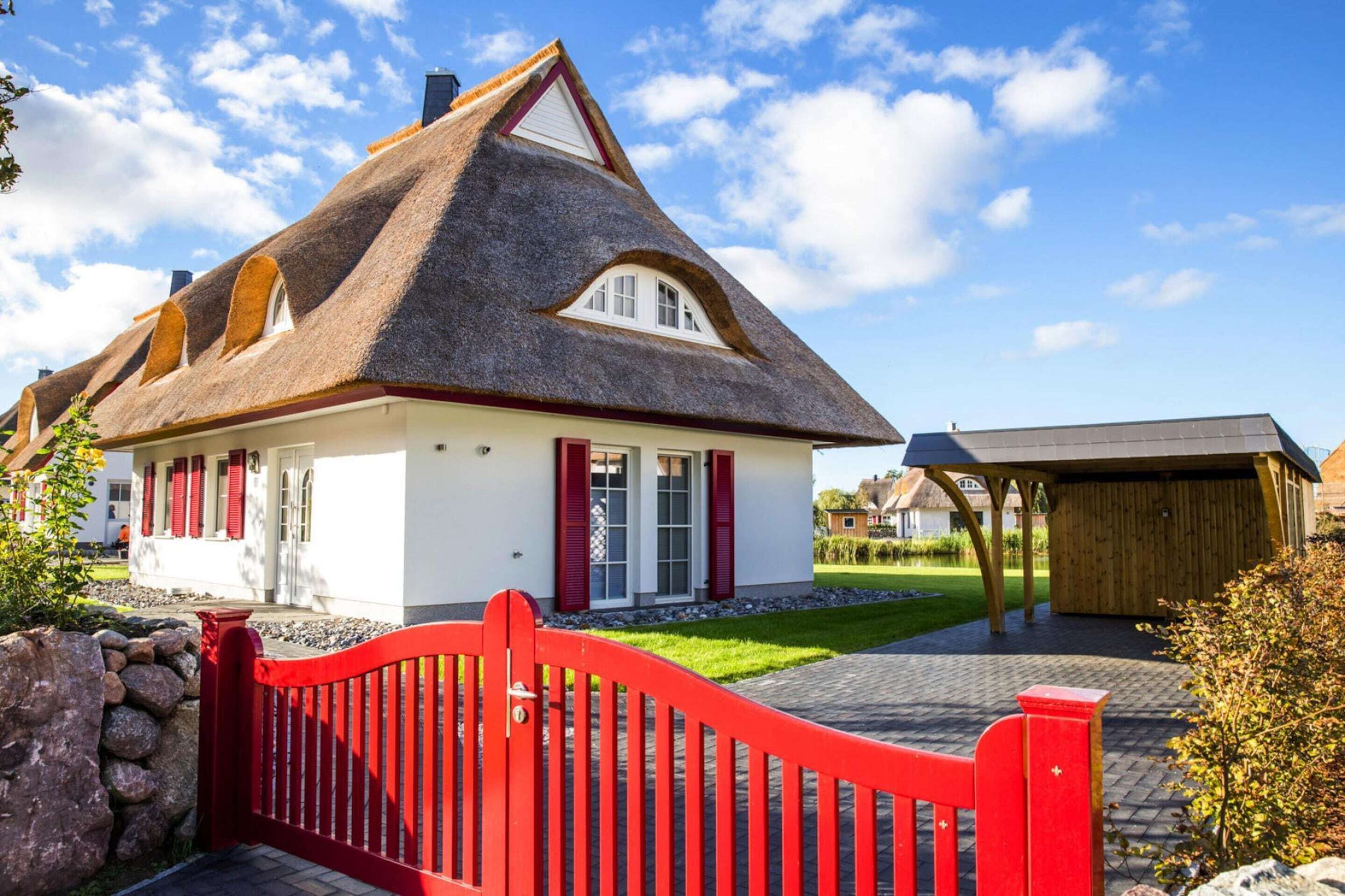Una casa con techo de paja, paredes blancas y contraventanas rojas.
