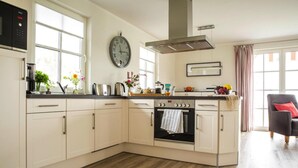 A modern kitchen with white cabinetry, a built-in oven, and a clock on the wall. - Ferienhaus in Fuhlendorf (Fuhlendorf)