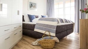 A bedroom with a bed, a wardrobe, a window, and a bedside table. - Ferienhaus in Fuhlendorf (Fuhlendorf)