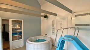 A room with a hot tub, a blue slide, and a door leading to another room. - Luxury Pool House by Sea - By Traum Ferienwohnungen (Ulfborg)