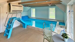 An indoor swimming pool with a slide, a chair, and a table. - Luxury Pool House by Sea - By Traum Ferienwohnungen (Ulfborg)
