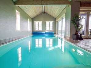 An indoor swimming pool with a wooden ceiling, large windows, and a blue bench. - 4 Star Holiday Home in Spottrup (Spøttrup)