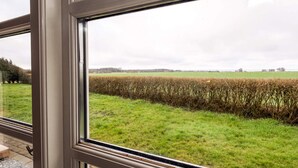 A view through a window with a metal frame, revealing a grassy field and a hedge. - 4 Star Holiday Home in Spottrup (Spøttrup)