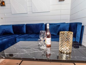 A modern living room with a dark marble coffee table, a bottle of wine, two wine glasses, and a decorative candle holder.