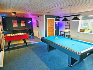 A pool table with a blue felt surface, a red foosball table, and a wooden door.