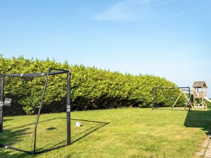 A soccer goal, a play area with a slide, and a wooden playhouse.