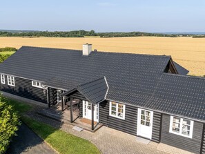 A large, dark wooden house with a sloped roof, a covered porch, and a view of a vast field. - 4 Star Holiday Home in Spottrup (Spøttrup)