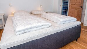 A double bed with a grey upholstered headboard, white bedding, and two bedside tables with wall-mounted lamps. - 4 Star Holiday Home in Spottrup (Spøttrup)