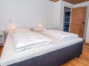 Cama doble con cabecera tapizada en gris, ropa de cama blanca y dos mesitas de noche con lámparas de pared.