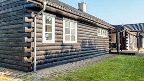 A log cabin with a chimney, a porch, and a window with a blue object on the windowsill. - 4 Star Holiday Home in Spottrup (Spøttrup)
