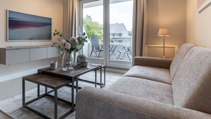 A modern living room with a sofa, a coffee table, a TV, and a window with curtains. - Renovierte Ferienwohnung, St. Peter-ording (St. Peter-Ording)