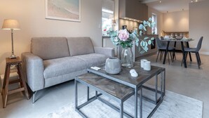 A modern living room with a sofa, coffee table, and dining area with chairs. - Renovierte Ferienwohnung, St. Peter-ording (St. Peter-Ording)