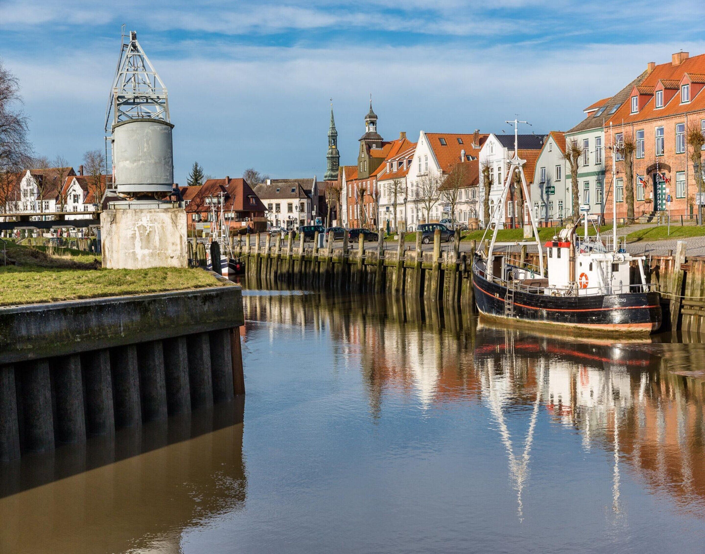 A calm river with a boat docked at the pier, surrounded by historic buildings with red-tiled roofs.