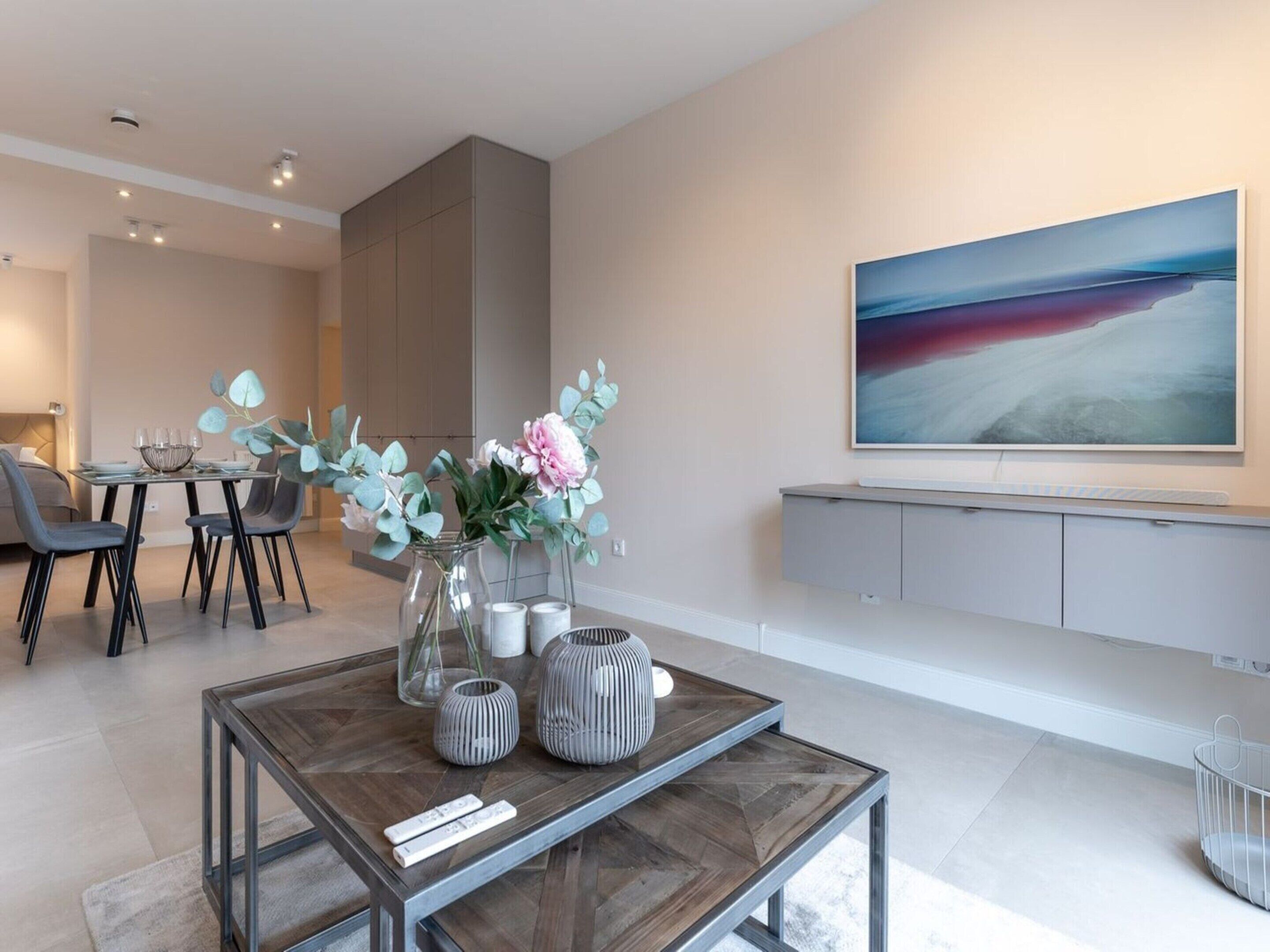 A modern living room with a dining area, a coffee table with decorative items, and a large abstract painting on the wall.