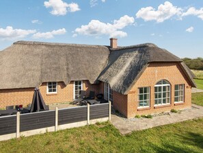 A thatched-roof cottage with a brick extension, outdoor seating, and a grassy yard.