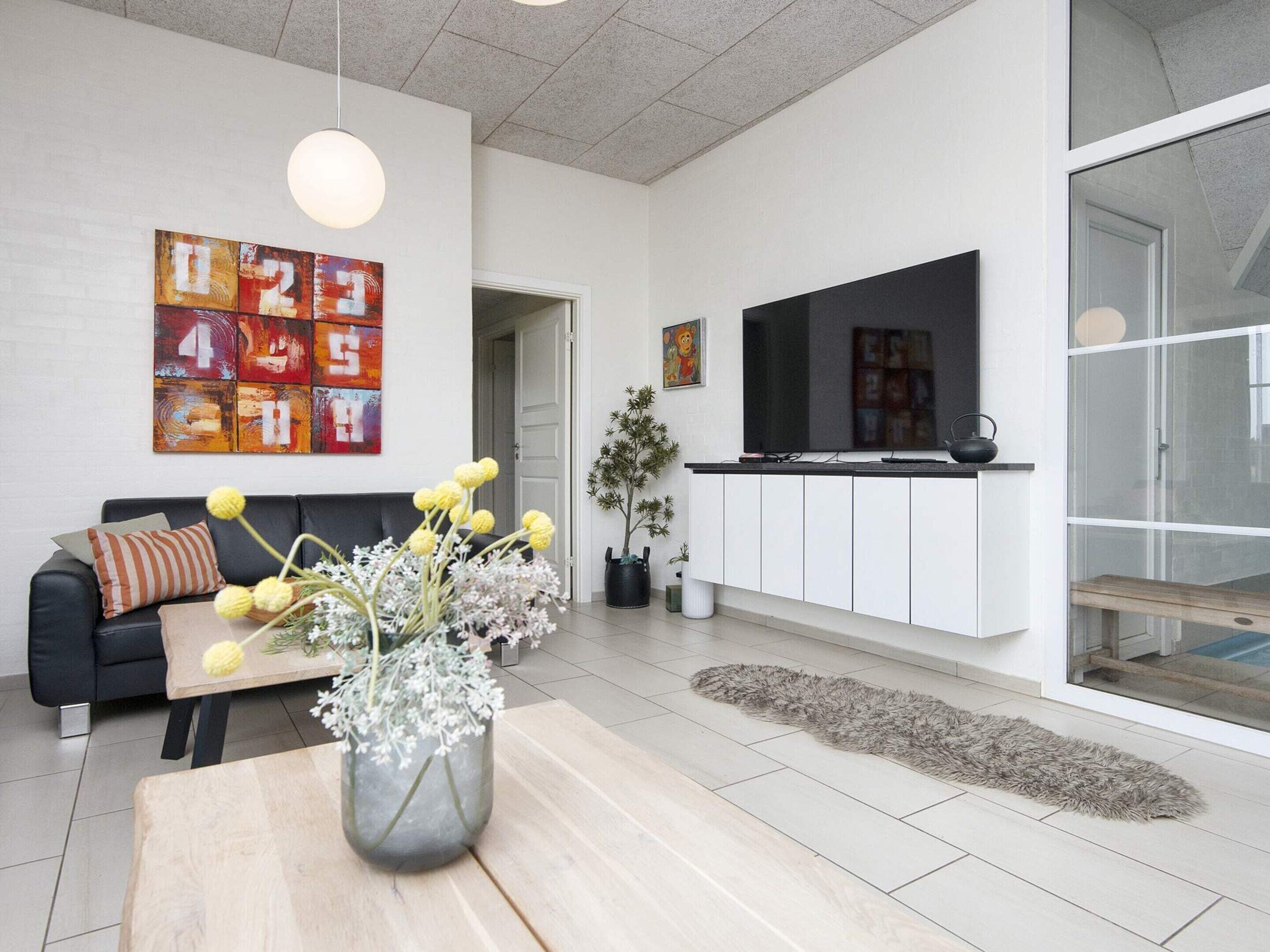 A modern living room with a sofa, a coffee table with a vase, a flat-screen TV, and artwork on the wall.
