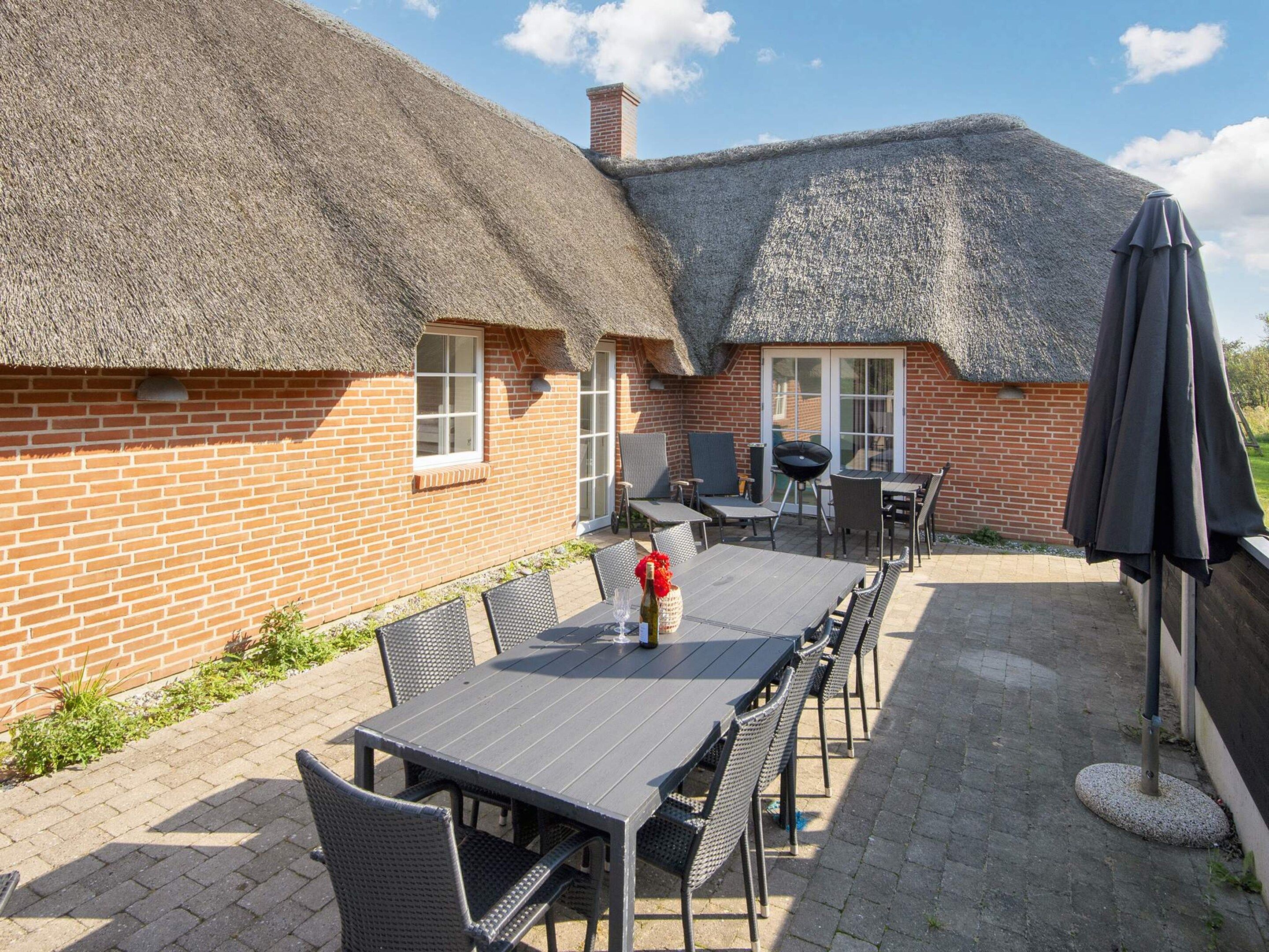 Ein Backsteinhaus mit einem Strohdach, einer Terrasse mit Tisch und Stühlen sowie einem Grill.