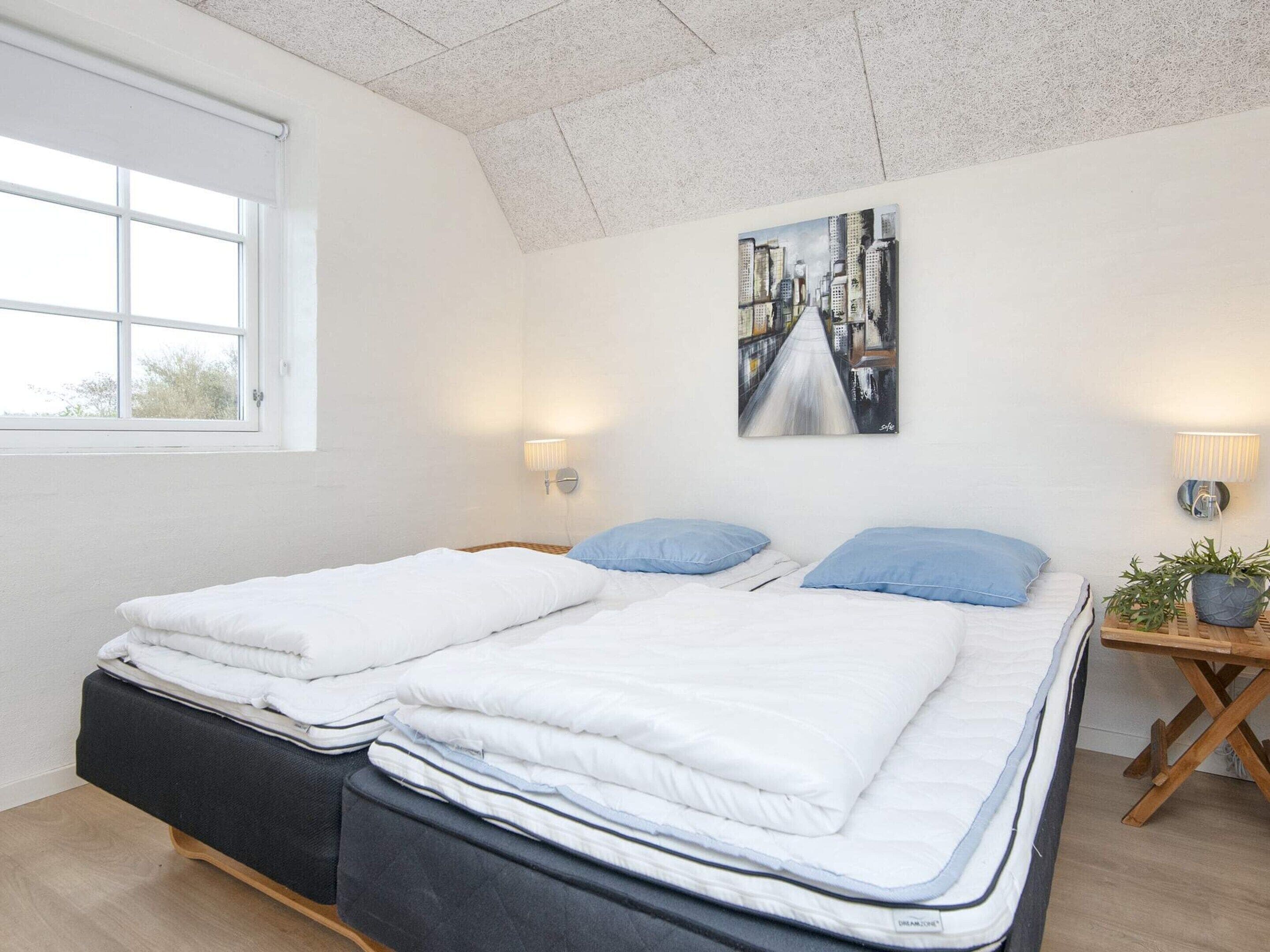 A bedroom with two beds, a window, a painting, and bedside lamps.