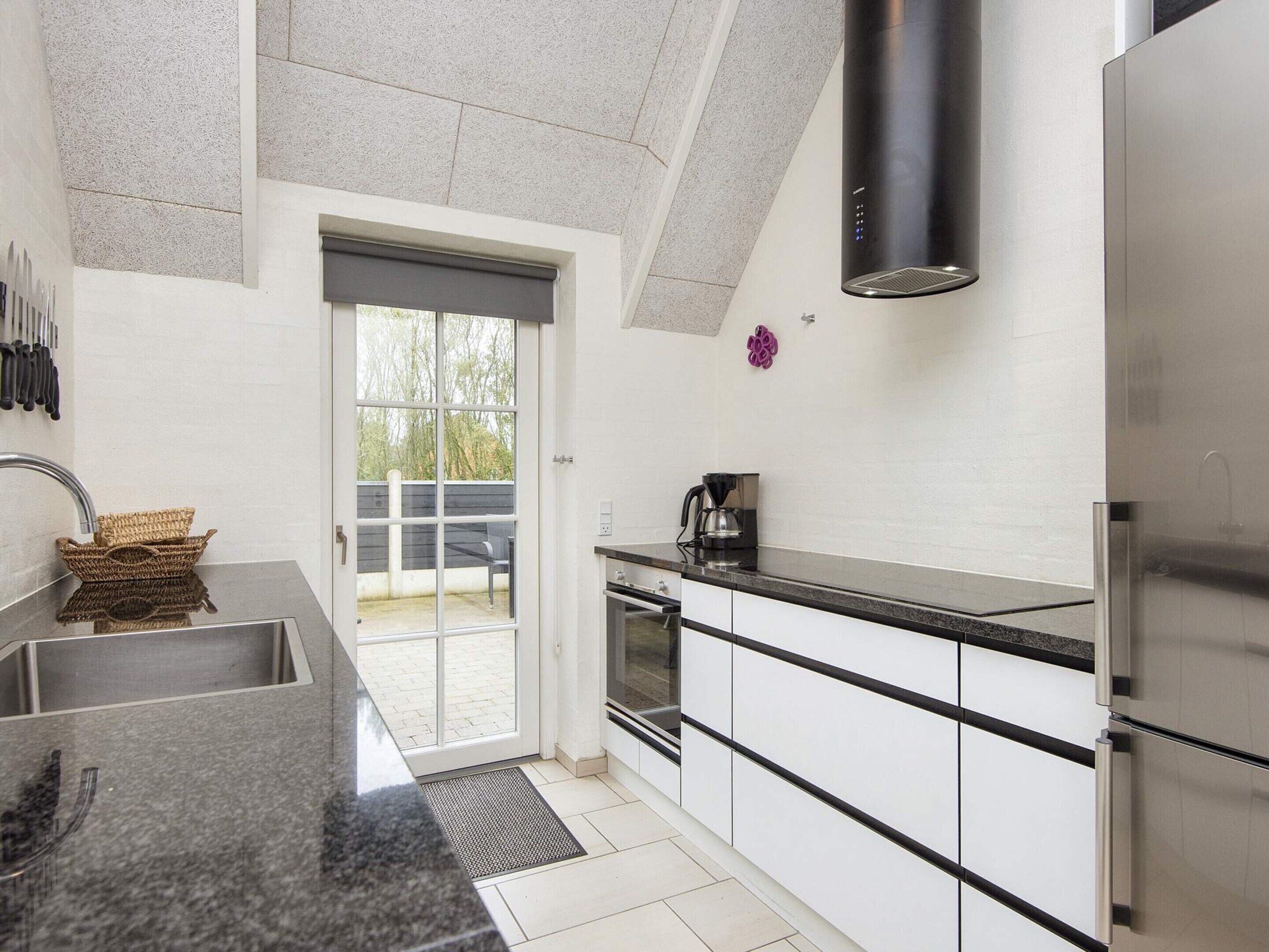 A modern kitchen with a stainless steel refrigerator, a coffee maker, and a window with a view of the outdoors.