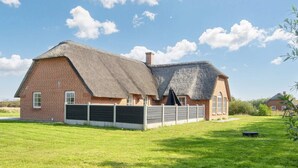 A brick house with a thatched roof, a fenced yard, and a grassy field. - 4 Star Holiday Home in Ulfborg (Ulfborg)