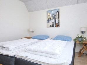 A bed with white bedding, two blue pillows, a cityscape painting on the wall, and a small plant on a wooden side table. - 4 Star Holiday Home in Ulfborg (Ulfborg)