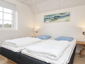 Une chambre avec deux lits, une fenêtre, un tableau et une lampe fixée au mur.