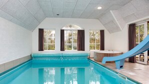 An indoor swimming pool with a slide, large windows, and a view of the outdoors. - 4 Star Holiday Home in Ulfborg (Ulfborg)