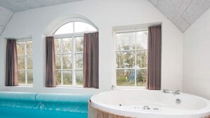A modern bathroom with a freestanding bathtub, a large window with curtains, and a view of a swimming pool. - 4 Star Holiday Home in Ulfborg (Ulfborg)