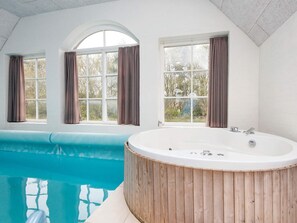 A modern bathroom with a freestanding bathtub, a large window with curtains, and a view of a swimming pool.