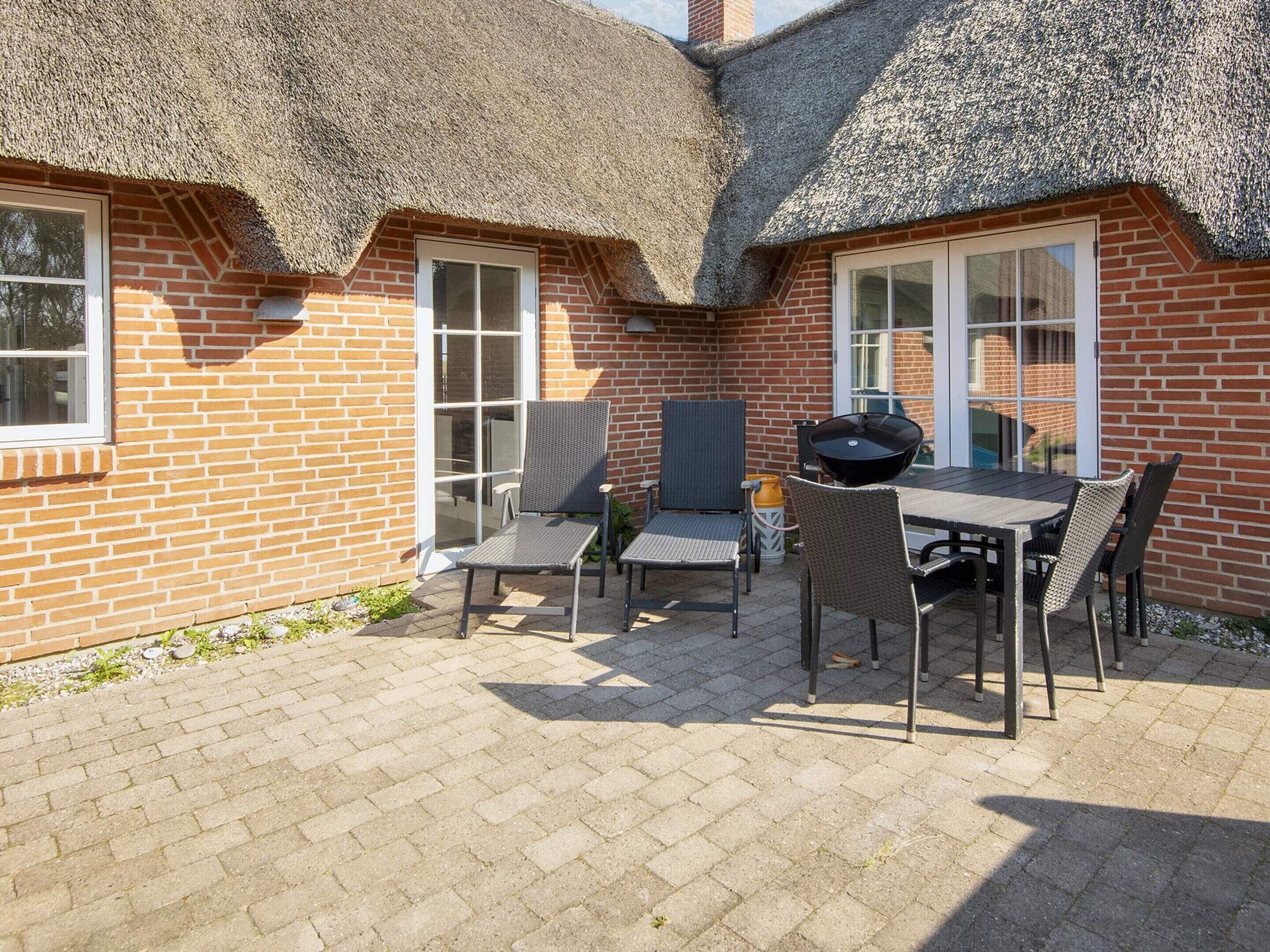 A patio with a brick wall, a thatched roof, and a table with chairs.