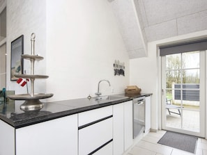 A modern kitchen with a built-in dishwasher, a sink, and a decorative metal stand. - 4 Star Holiday Home in Ulfborg (Ulfborg)