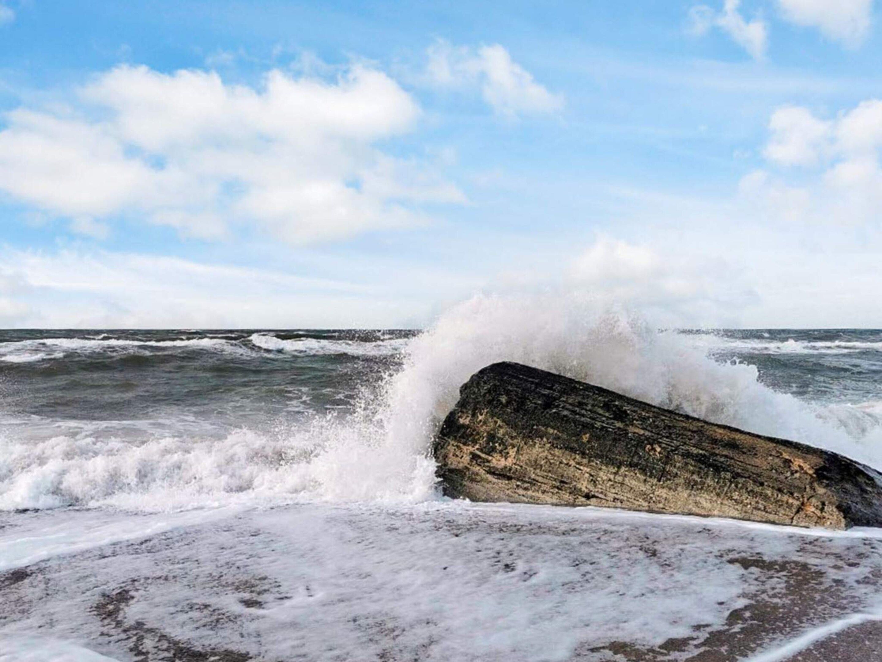 A large rock by the sea with waves crashing against it.
