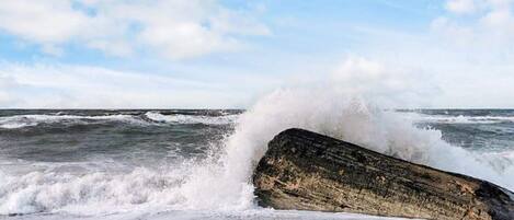 A large rock by the sea with waves crashing against it.