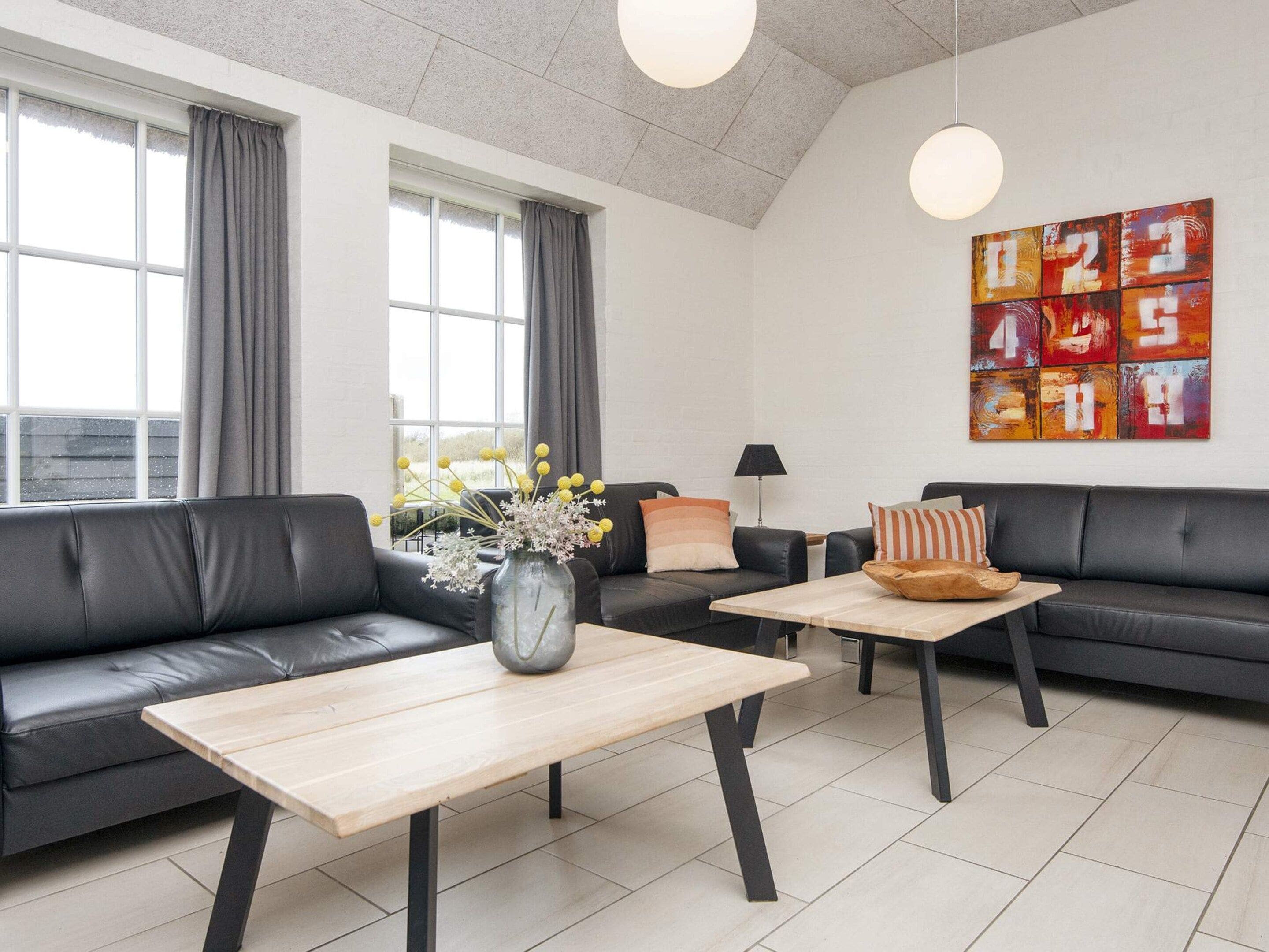 Una sala de estar moderna con un sofá de cuero negro, una mesa de centro de madera y un jarrón decorativo.