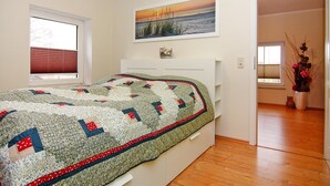 A bedroom with a bed, a painting above the bed, and a window with blinds. - Doppelhaushaelfte, Tankenhagen (Dassow)
