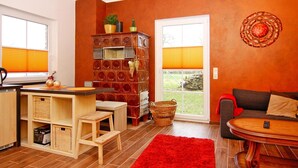 A living room with a red rug, a wooden coffee table, a sofa, and a kitchen area with a wooden cabinet and wicker baskets. - Doppelhaushaelfte, Tankenhagen (Dassow)