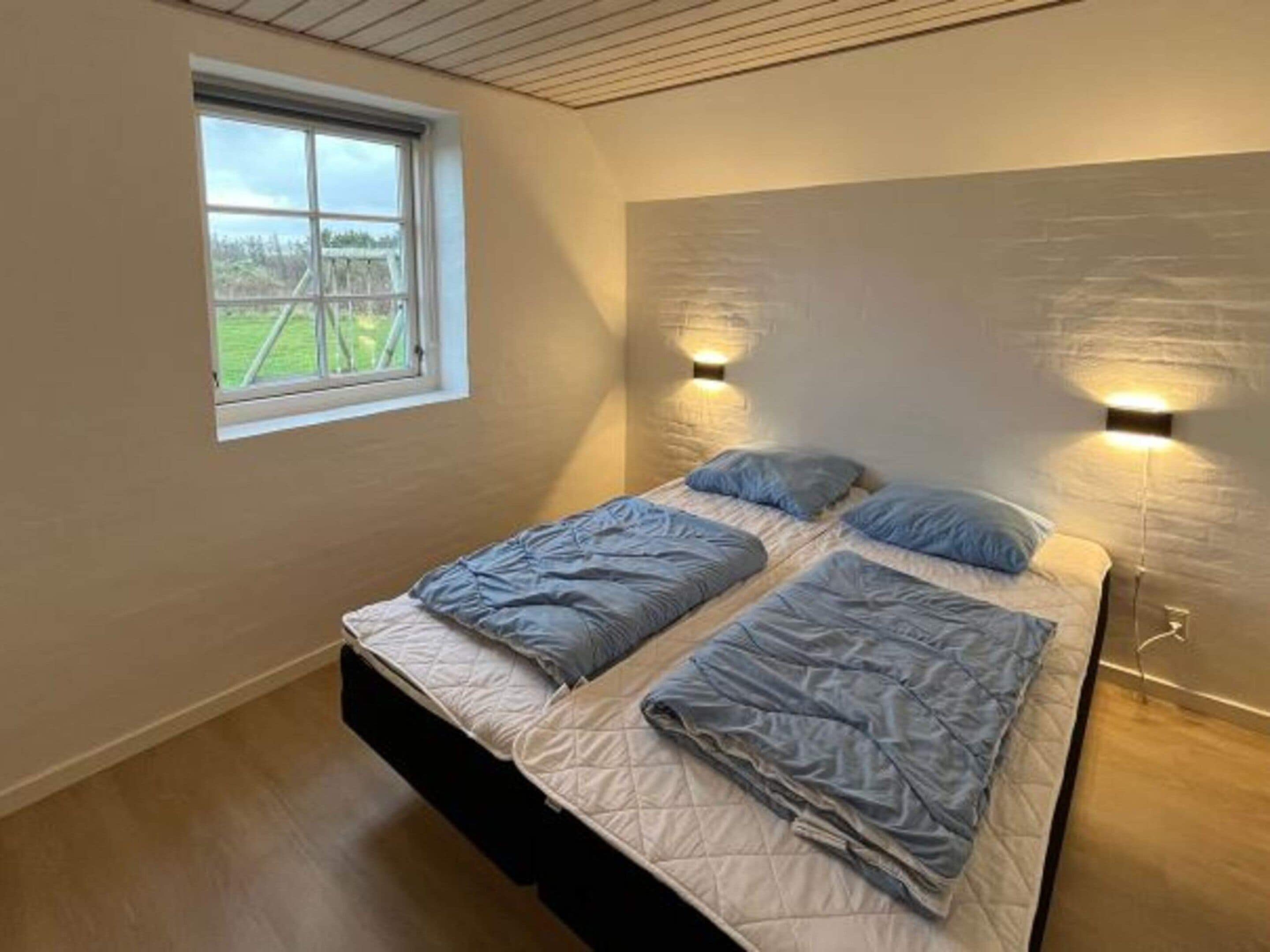 Un dormitorio con un ventanal grande, dos camas e iluminación empotrada.