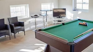 A pool table with a green felt surface, a pool cue, and billiard balls. There are two chairs and a small table with a television in the background. - 4 Star Holiday Home in Ulfborg (Ulfborg)