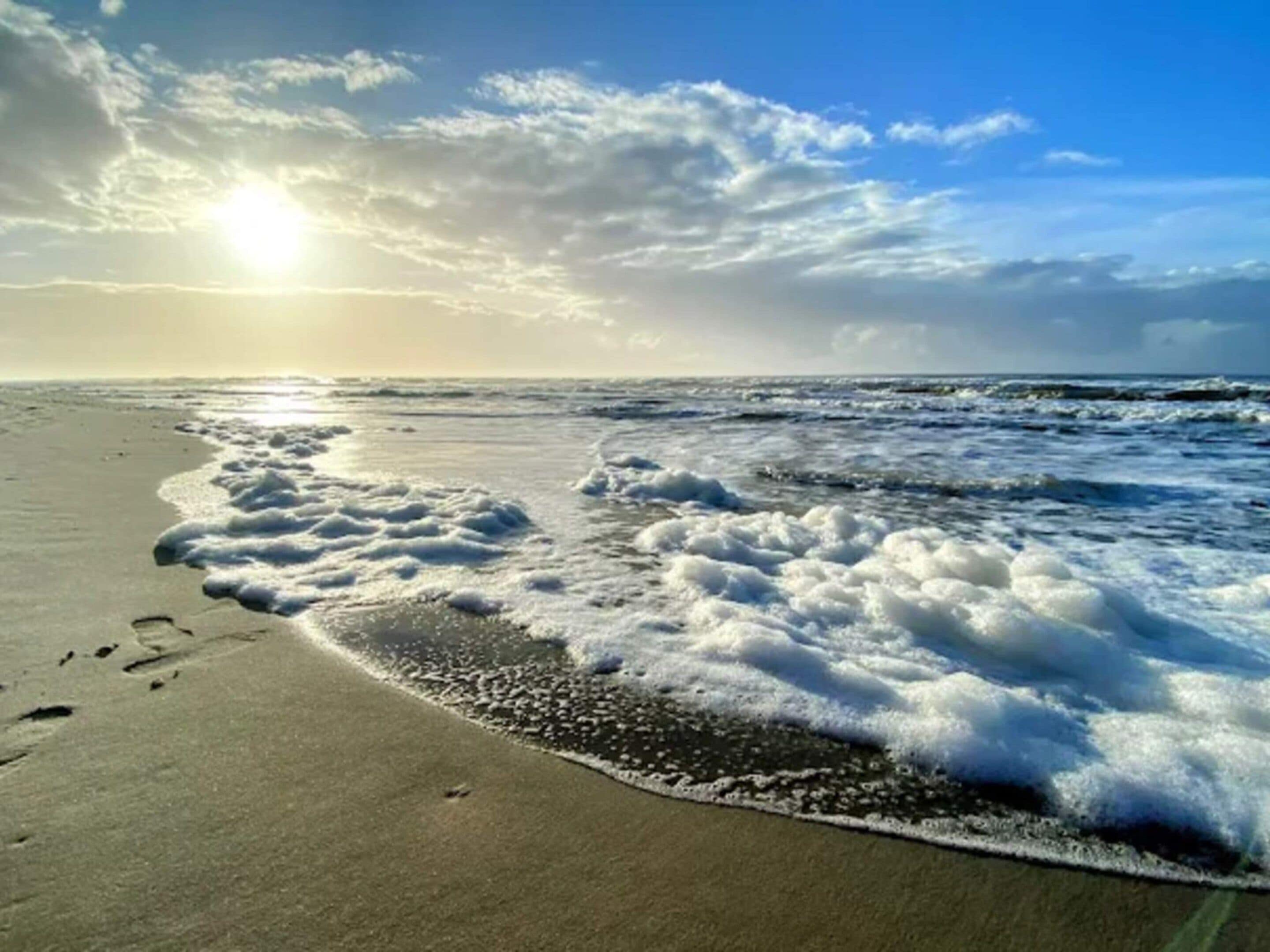 A beach with waves, footprints, and a clear sky.
