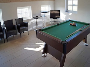 A pool table with a green felt surface, surrounded by chairs and a television.