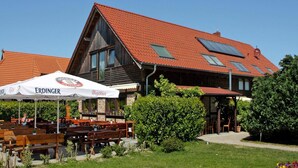 A traditional wooden building with a red-tiled roof and multiple skylights. There are outdoor seating areas with wooden benches and tables, and a white umbrella with "ERDINGER" branding. - Apartment for up to 6 People in Lepels Hof (Luetow)
