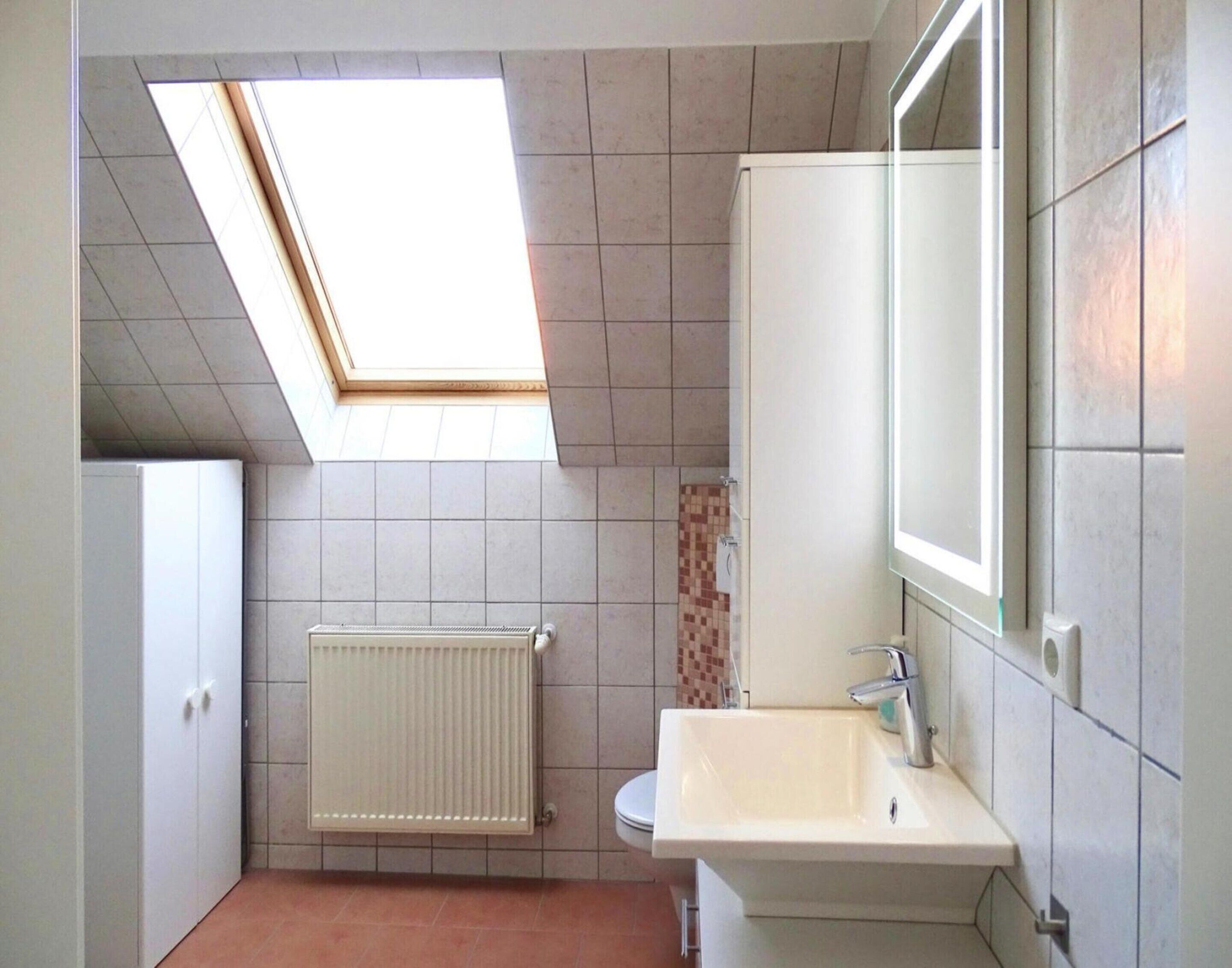 A small, modern bathroom with a skylight, a radiator, a sink, and a toilet.