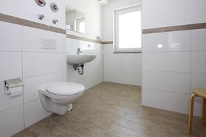 A bathroom with a toilet, sink, mirror, and a window. - Appartement Hafenflair am Plauer See (Plau am See)