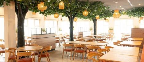 Un restaurante con mesas y sillas redondas, plantas de interior y luces colgantes.