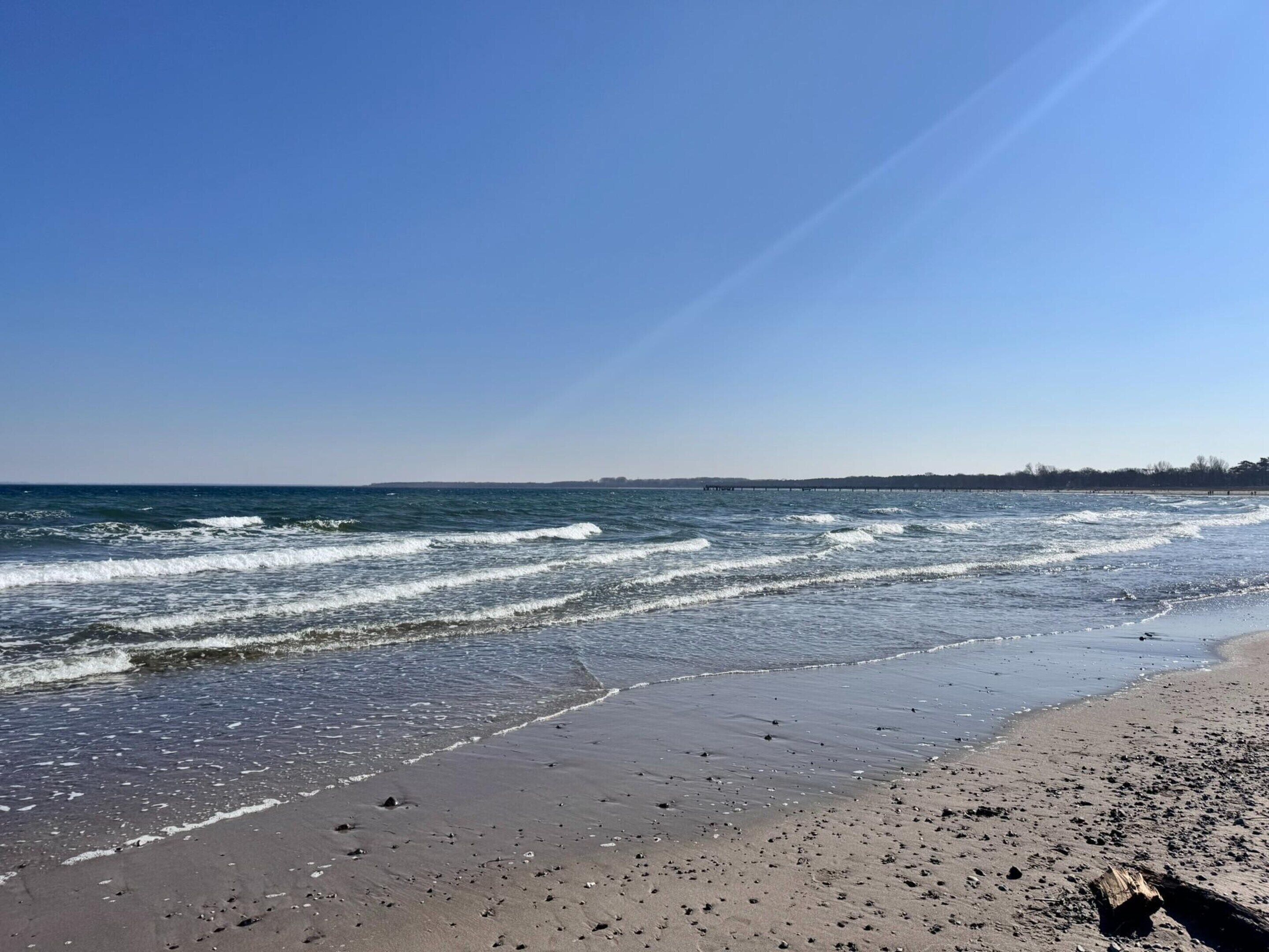 A beach with waves, a clear sky, and a distant shoreline.