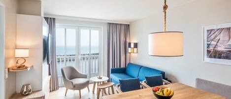 Una camera d'albergo moderna con un tavolo da pranzo in legno, un divano blu e un balcone vista mare.