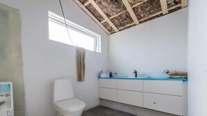 Un baño con inodoro blanco, lavabo con encimera azul y ventana sobre el lavabo.